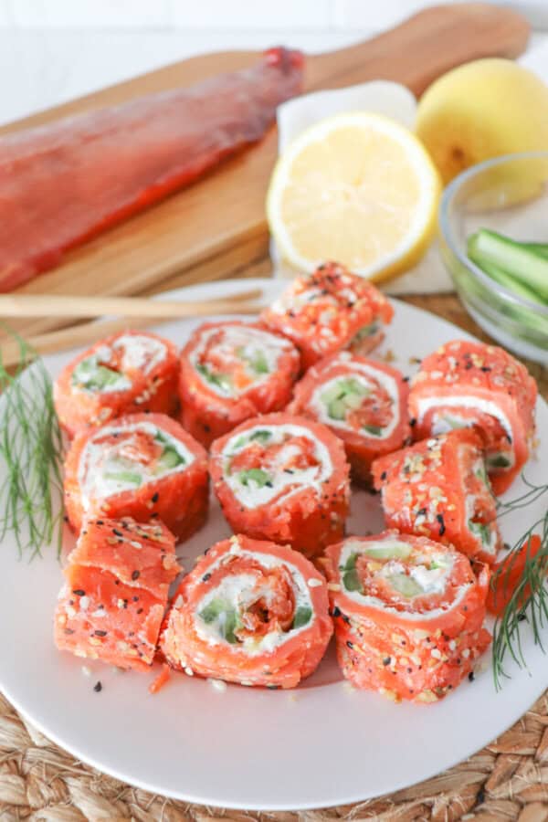 Smoked salmon rolled around cream cheese, cucumbers and avocado and cut into sushi style rolls on a white plate.