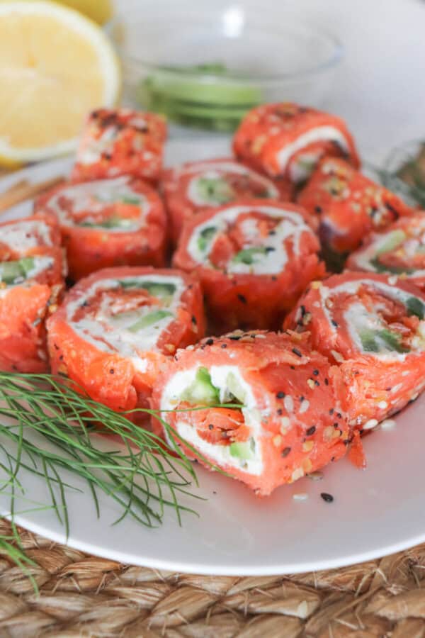 Smoked salmon rolled around cream cheese, cucumbers and avocado and cut into sushi style rolls on a white plate.