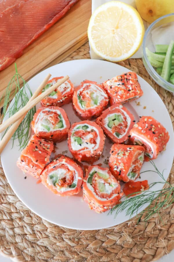 Smoked salmon rolled around cream cheese, cucumbers and avocado and cut into sushi style rolls on a white plate.