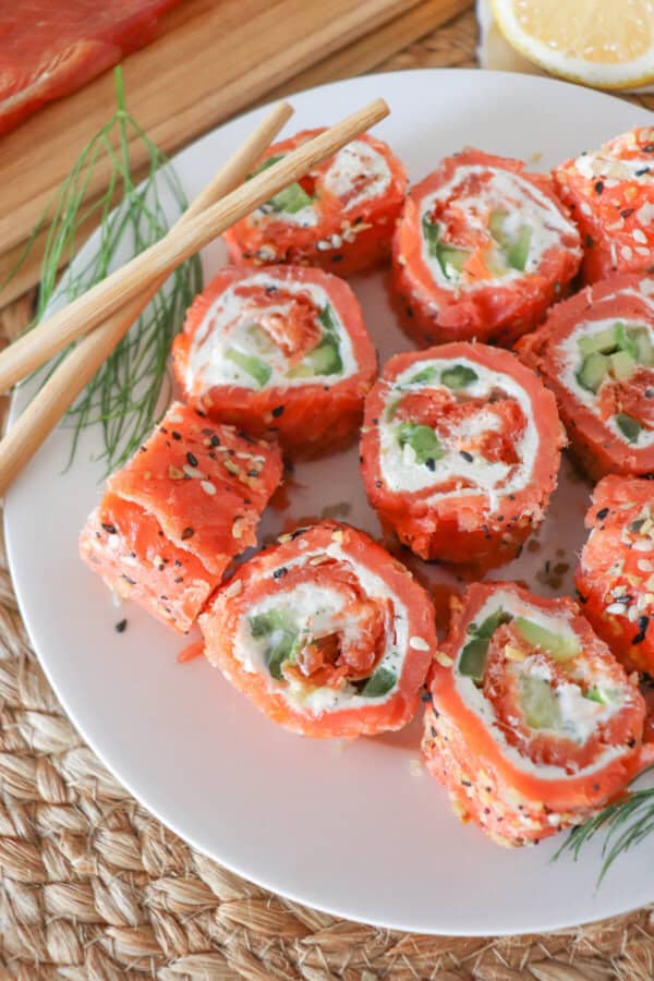 Smoked salmon rolled around cream cheese, cucumbers and avocado and cut into sushi style rolls on a white plate.