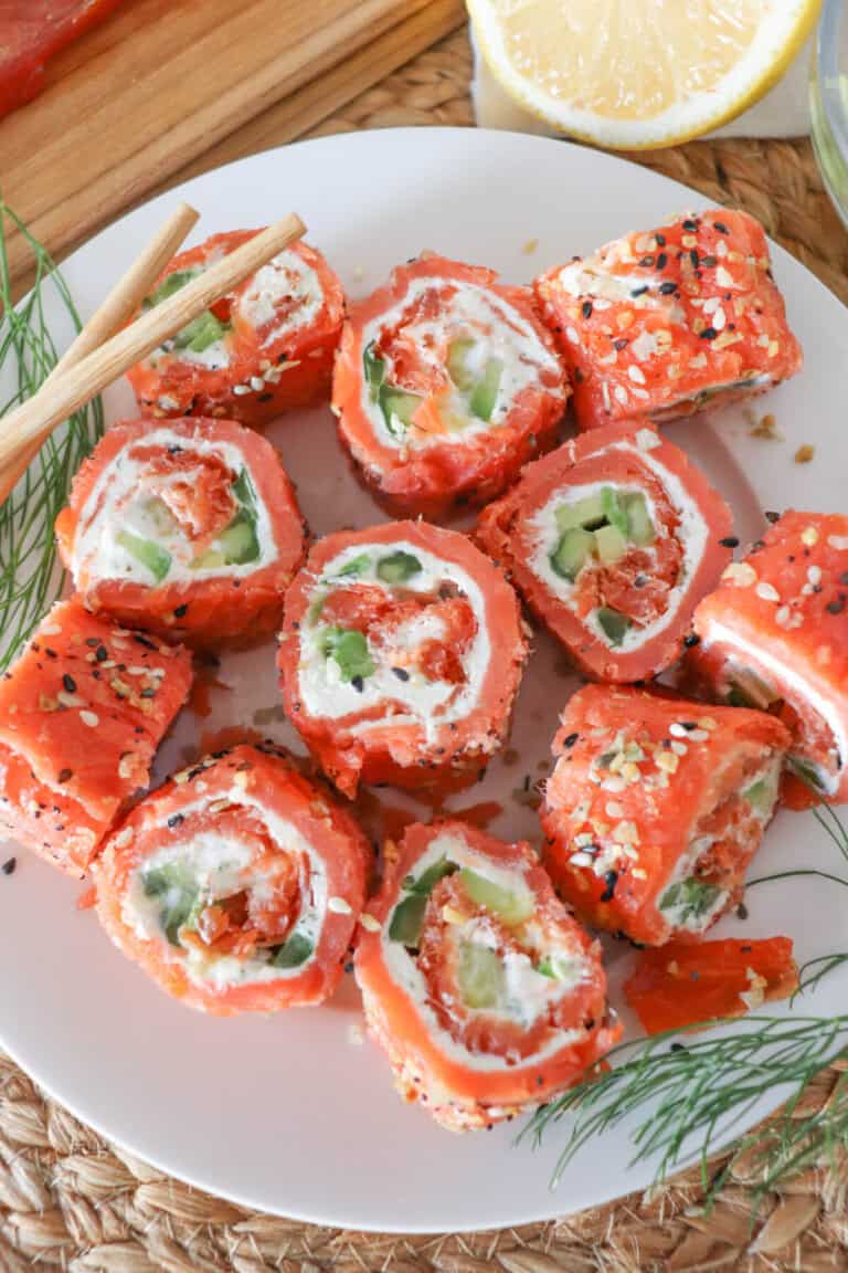 Smoked salmon rolled around cream cheese, cucumbers and avocado and cut into sushi style rolls on a white plate.