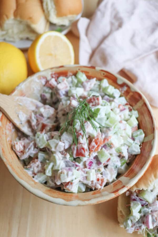 Diced celery, red onion and smoked salmon covered in creamy white mayonnaise in a clay bowl with a sprig of fresh dill on top.