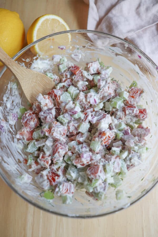 Ingredients for smoked salmon salad mixed in a clear glass bowl.