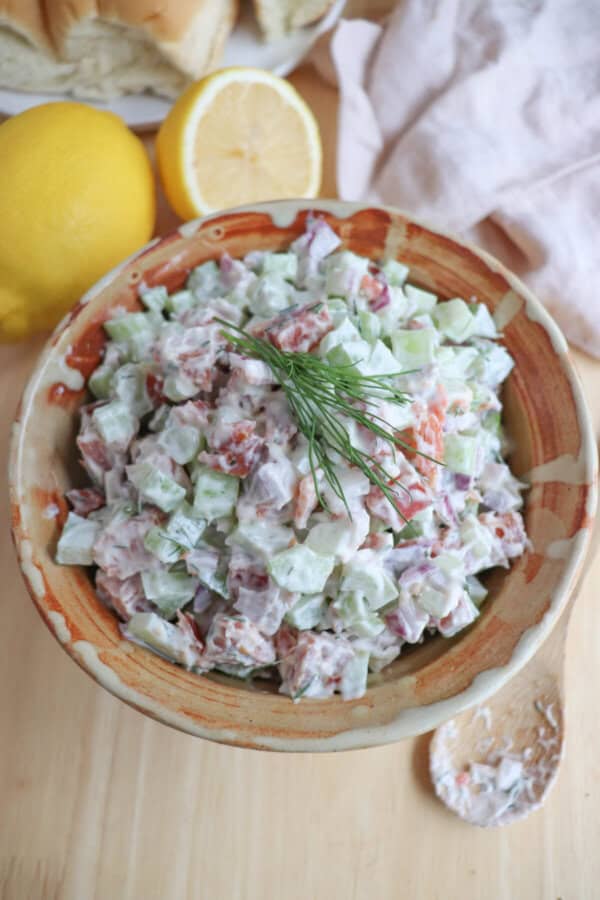 Diced celery, red onion and smoked salmon covered in creamy white mayonnaise in a clay bowl with a sprig of fresh dill on top.