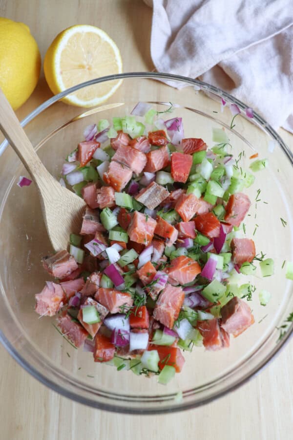 Ingredients for smoked salmon salad combined in a clear glass bowl.