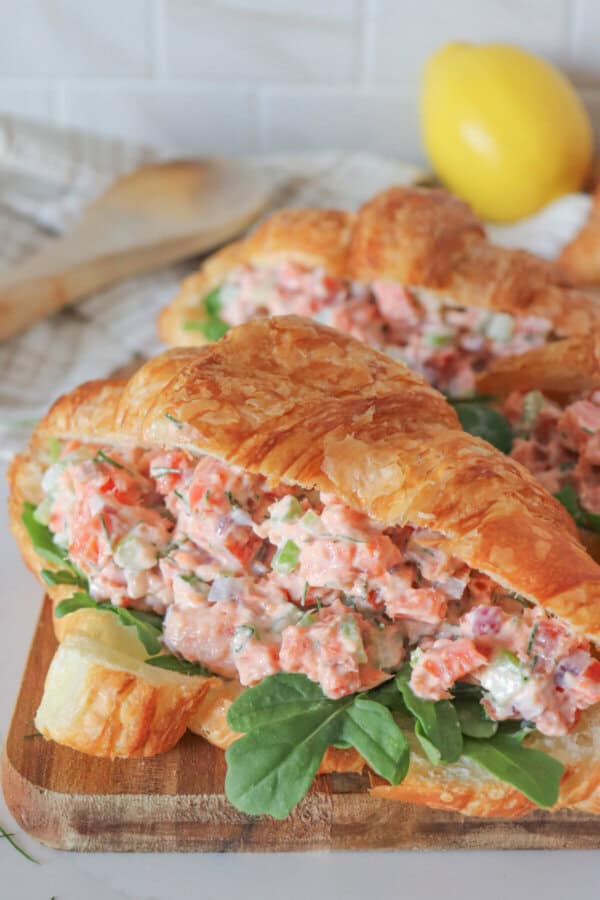 Smoked salmon salad in a fresh croissant with arugula on a wooden cutting board.