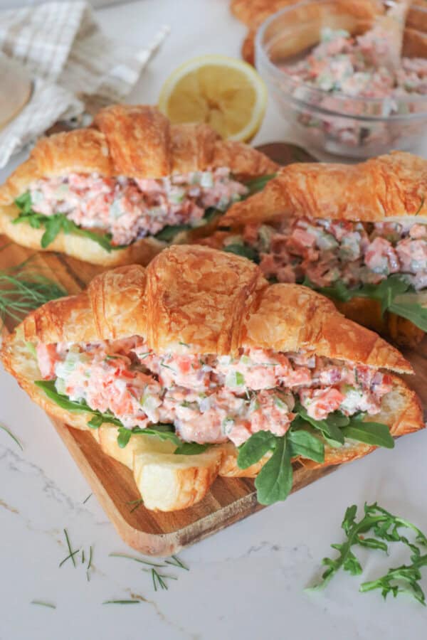 Smoked salmon salad in a fresh croissant with arugula on a wooden cutting board.
