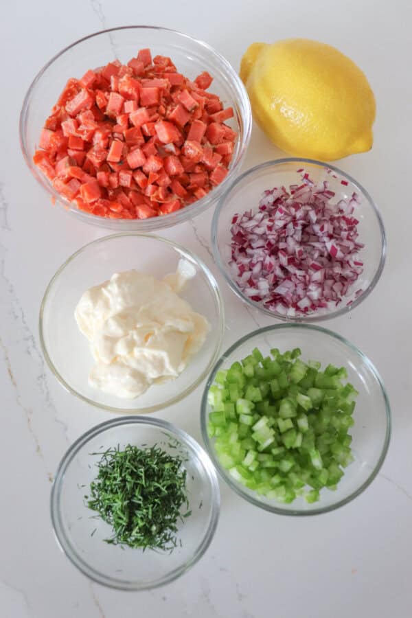 Ingredients for smoked salmon sandwiches in clear glass bowls on a white counter.