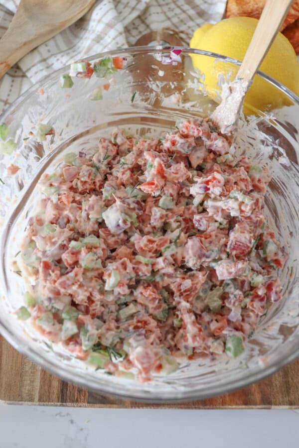 Ingredients for smoked salmon salad mixed together in a clear glass bowl.