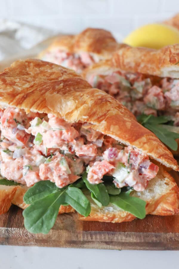 Smoked salmon salad in a fresh croissant with arugula on a wooden cutting board.