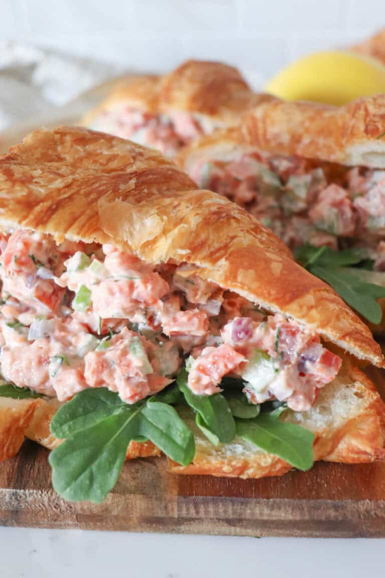 Smoked salmon salad in a fresh croissant with arugula on a wooden cutting board.