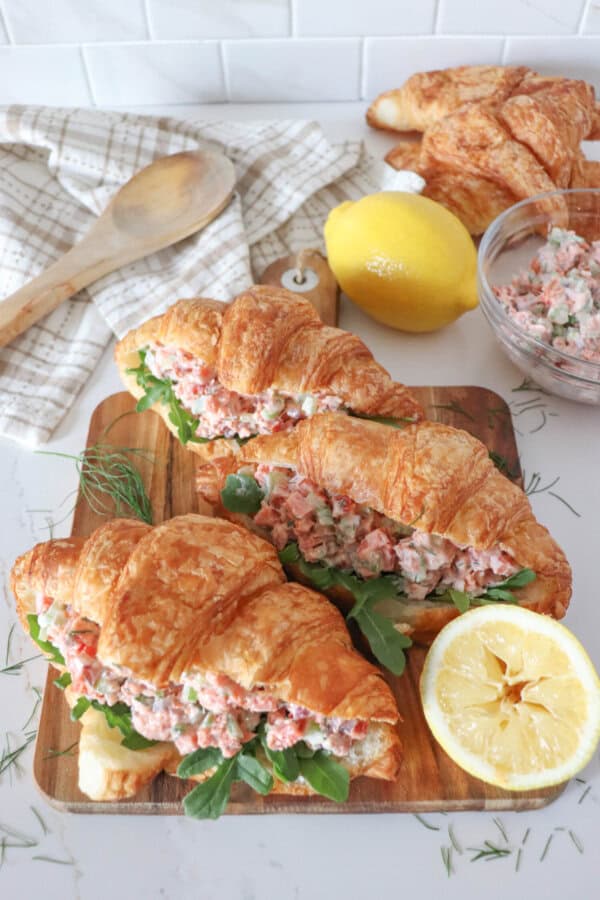 Smoked salmon salad in a fresh croissant with arugula on a wooden cutting board.