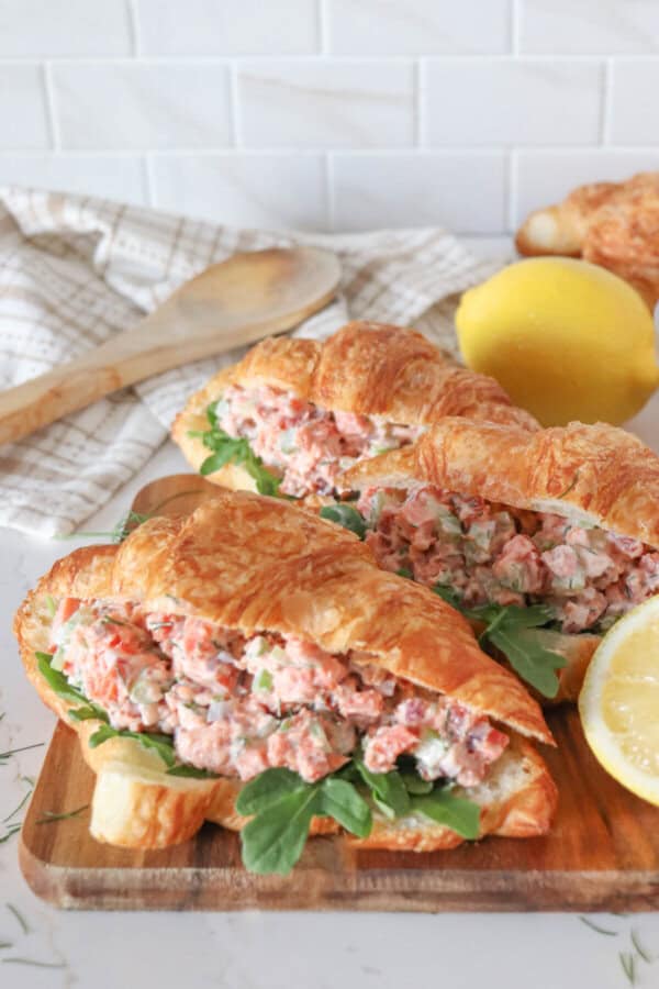 Smoked salmon salad in a fresh croissant with arugula on a wooden cutting board.