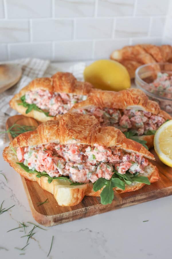 Smoked salmon salad in a fresh croissant with arugula on a wooden cutting board.