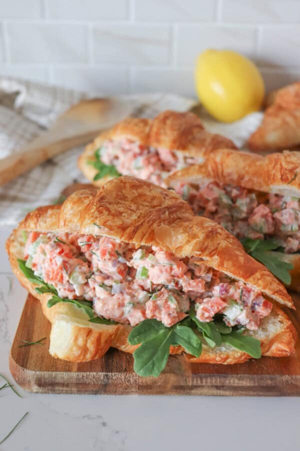 Smoked salmon salad in a fresh croissant with arugula on a wooden cutting board.