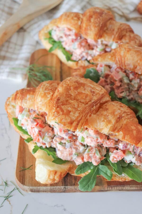 Smoked salmon salad in a fresh croissant with arugula on a wooden cutting board.