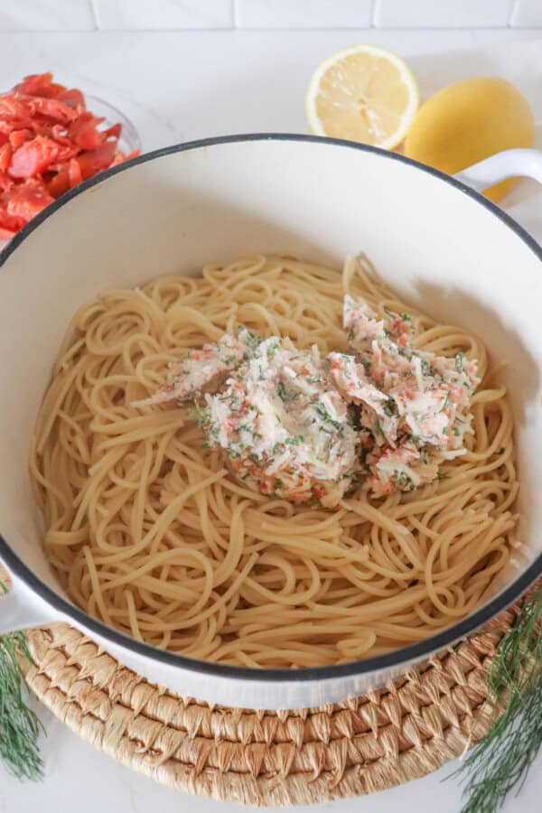 Cooked spaghetti in a white dutch oven with butter sauce on top.
