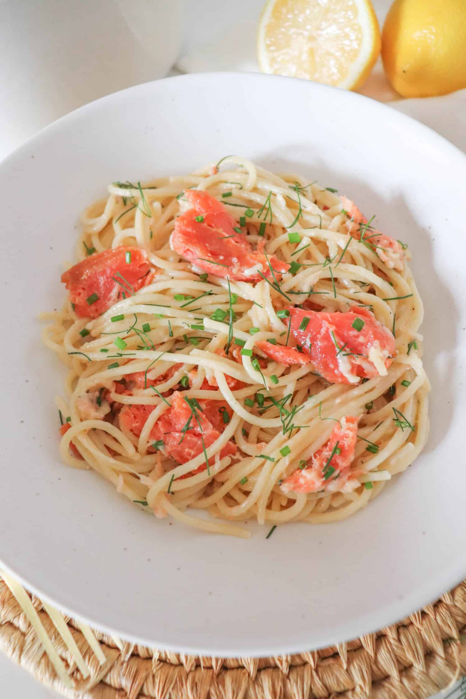 Cooked spaghetti noodles topped with pieces of smoked salmon and garnished with fresh dill in a white bowl.