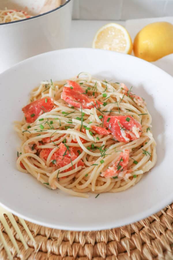 Cooked spaghetti noodles topped with pieces of smoked salmon and garnished with fresh dill in a white bowl.