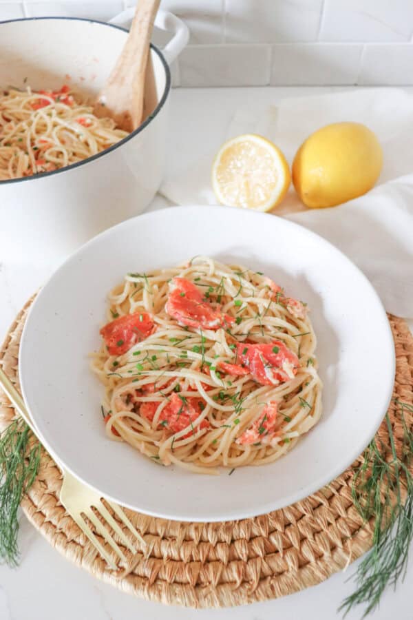 Cooked spaghetti noodles topped with pieces of smoked salmon and garnished with fresh dill in a white bowl.