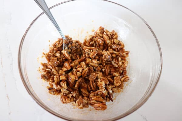 Pecans and brown sugar mixed in a clear glass bowl.