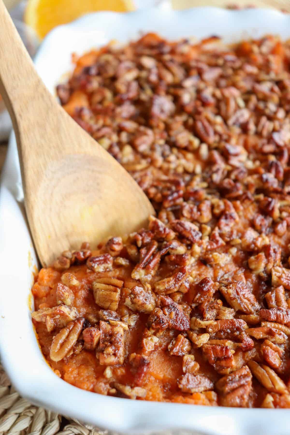 Sweet potato casserole with streusel topping with a wooden spoon scooping from a white casserole dish.