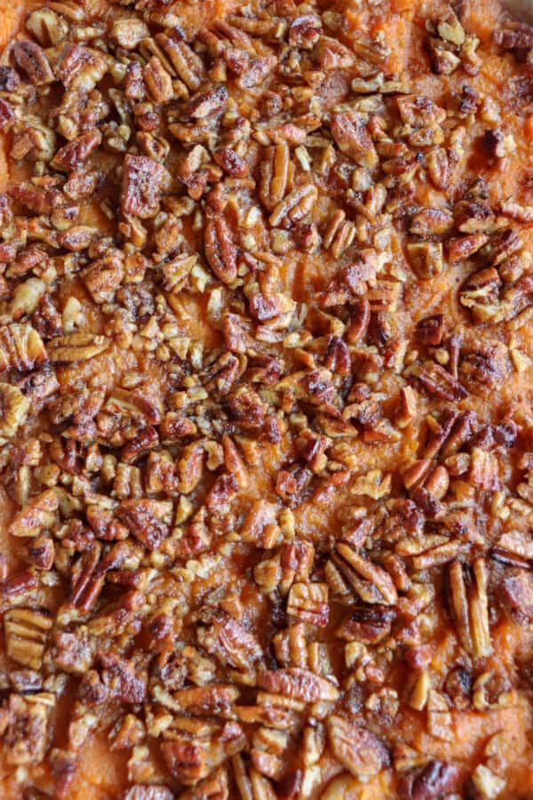 Close up of Sweet potato casserole topped with a caramel pecan streusel in a white casserole dish.