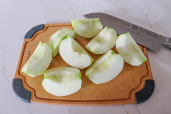 Granny smith apples peeled and cored on a cutting board.
