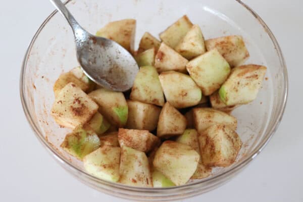 Apples cubes and coated in cinnamon in a clear glass bowl with a spoon in it.