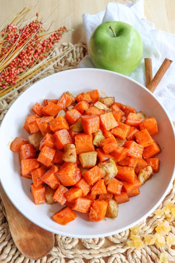 Cooked sweet potato and apple cubed covered in cinnamon in a large white bowl.