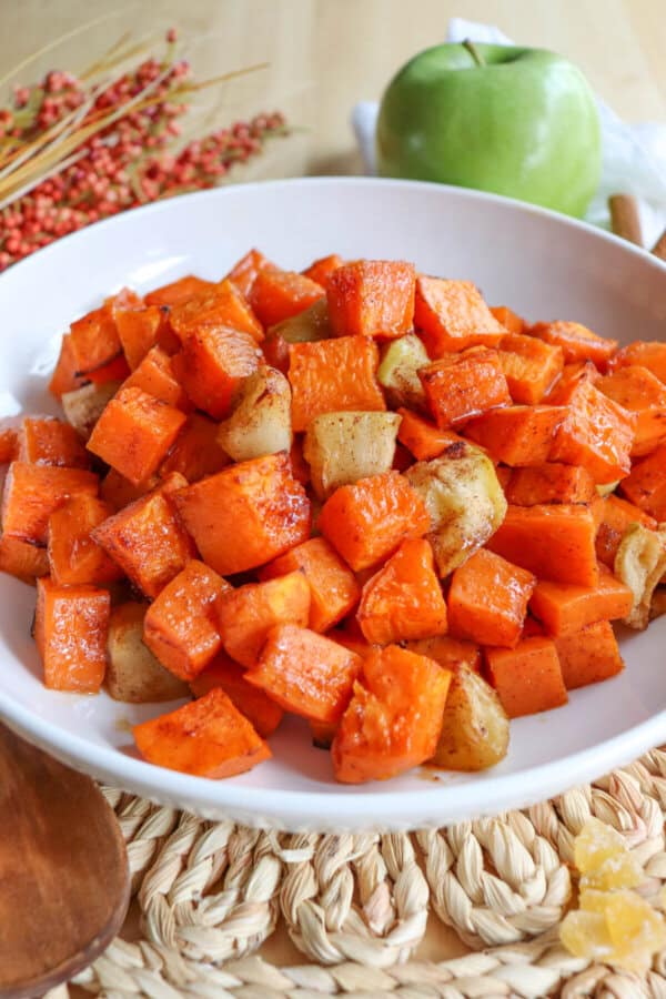 Cooked sweet potato and apple cubed covered in cinnamon in a large white bowl.