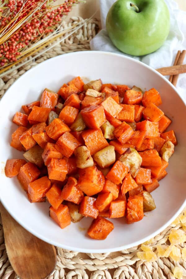 Cooked sweet potato and apple cubed covered in cinnamon in a large white bowl.