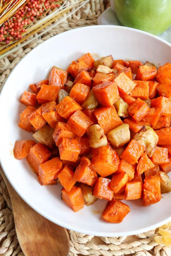 Cooked sweet potato and apple cubed covered in cinnamon in a large white bowl.