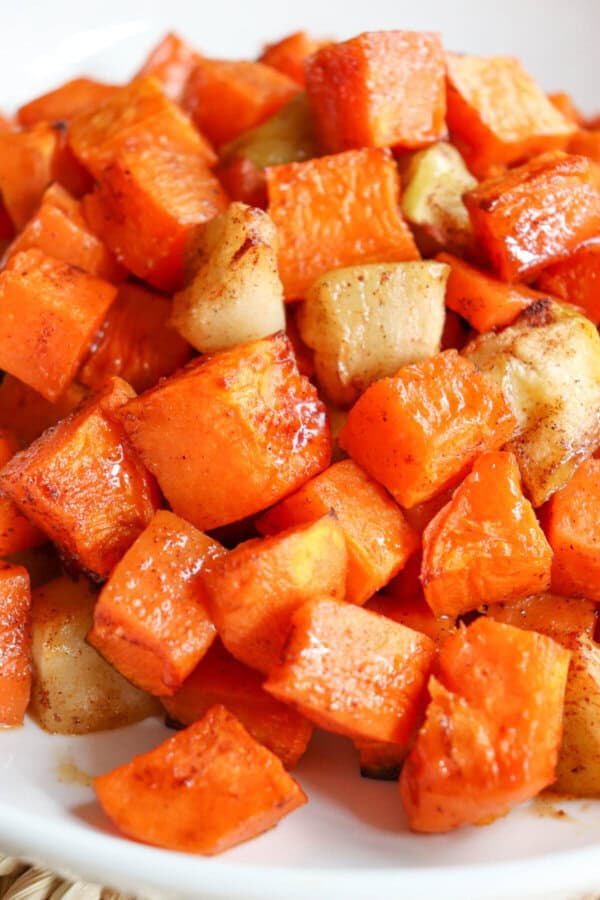 Close up of cooked sweet potato and apple cubed covered in cinnamon in a large white bowl.