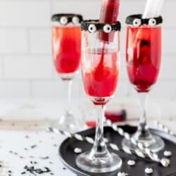 Red drinks in tall cocktail glasses with black rims and candy eyes.