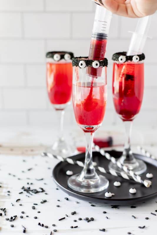 Red drinks in tall cocktail glasses with black rims and candy eyes.