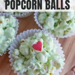 Green popcorn balls in white cupcake liners with red candy hearts on a wooden tray.