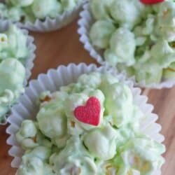 Green popcorn balls in white cupcake liners topped with a red candy heart.