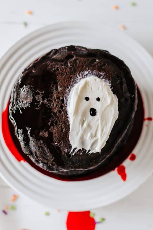 Stack of black pancakes with red syrup and white frosting in the shape of a ghost.