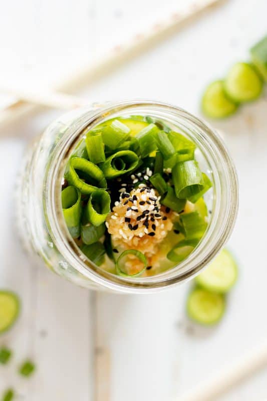 Mason jar with cucumber slices and minced garlic and green onion in it.