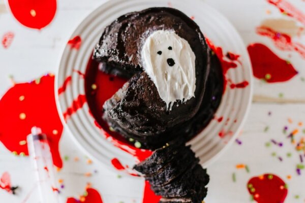 Stack of black pancakes with red syrup and white frosting in the shape of a ghost.