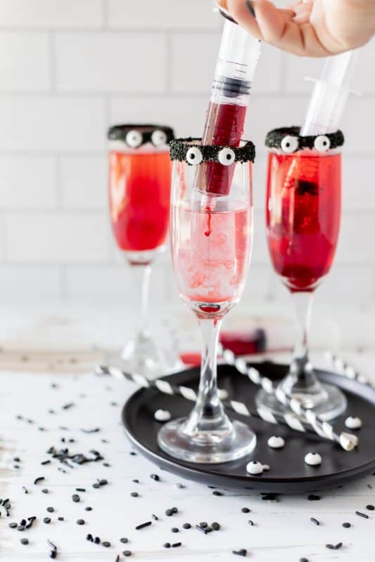 Red drinks in tall cocktail glasses with black rims and candy eyes.
