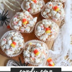 Popcorn balls with Halloween sprinkles and candy corn in cupcake liners on a wooden cutting board.
