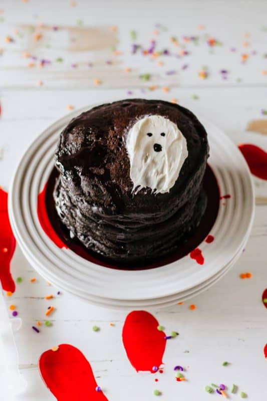 Stack of black pancakes with red syrup and white frosting in the shape of a ghost.