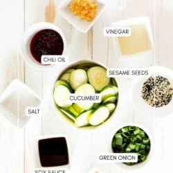 Ingredients for cucumber salad in small bowls on a white table.