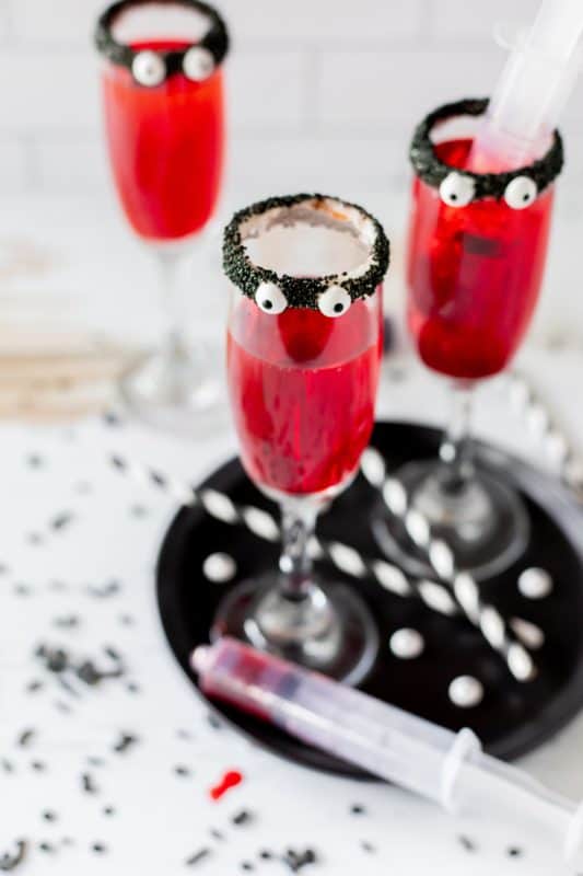 Red drinks in tall cocktail glasses with black rims and candy eyes.