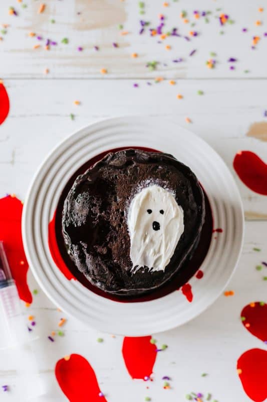 Stack of black pancakes with red syrup and white frosting in the shape of a ghost.