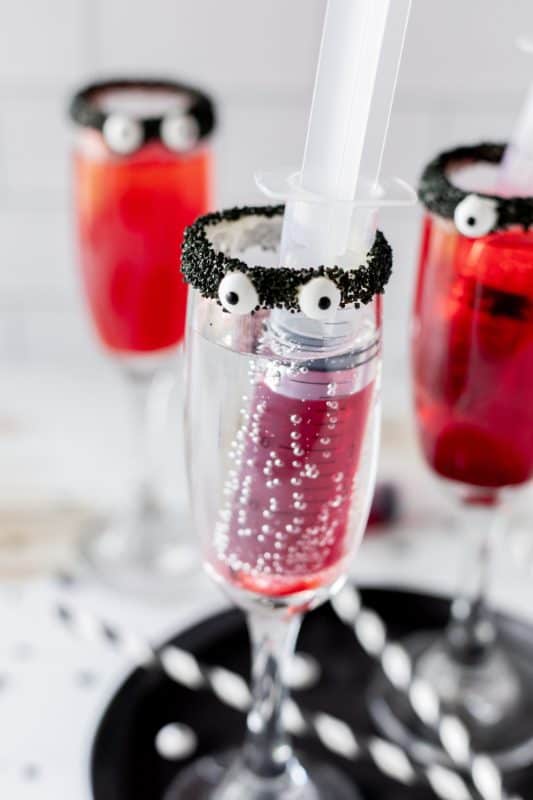 Red drinks in tall cocktail glasses with black rims and candy eyes.