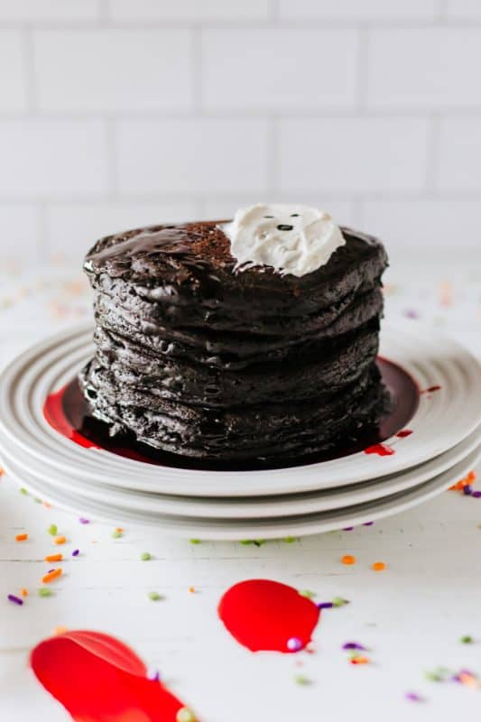 Stack of black pancakes with red syrup and white frosting in the shape of a ghost.