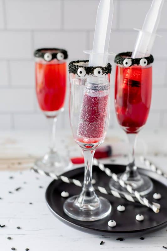 Red drinks in tall cocktail glasses with black rims and candy eyes.